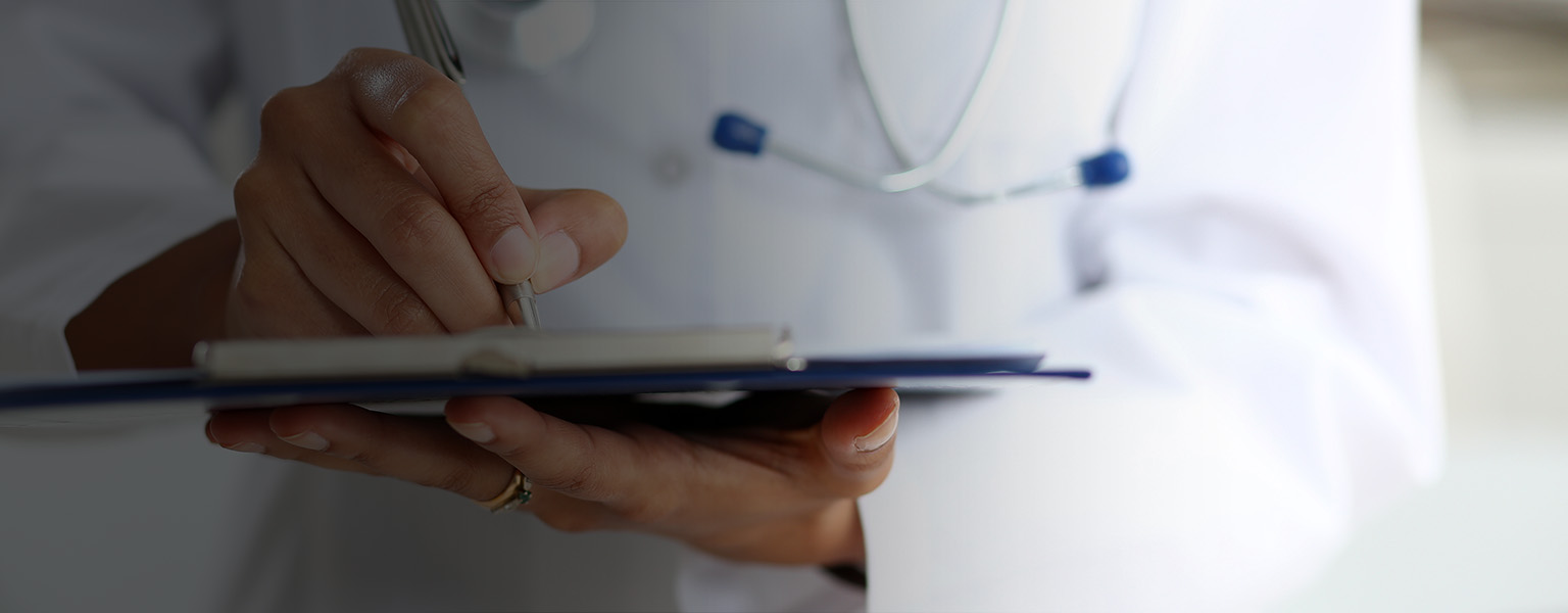 Doctor in lab coat writing in a clipboard.