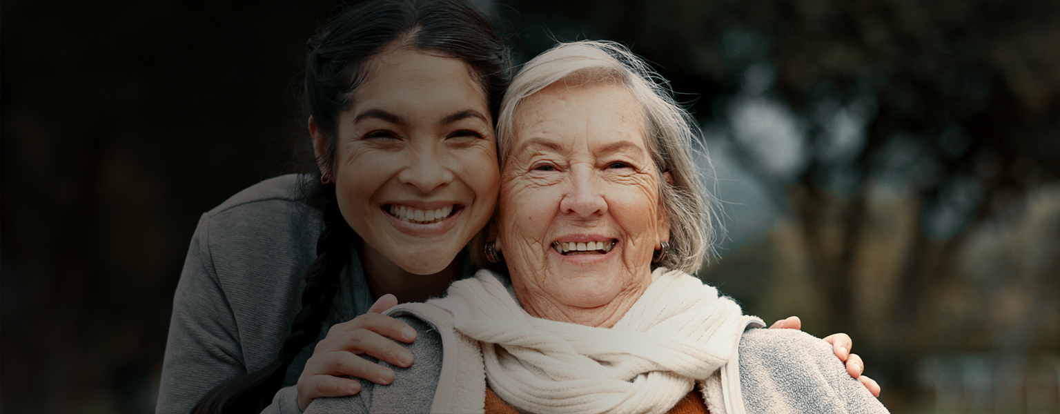 Persona adulta mayor sonriendo junto a su cuidadora.