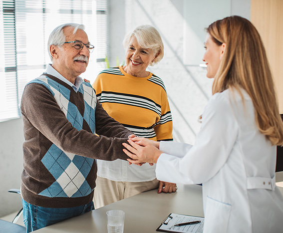 Senior couple shake hands with a caregiver.